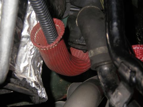 1990 Ford Bronco - Close-up view of engine components, including a red hose and black conduit, with silver insulation visible.