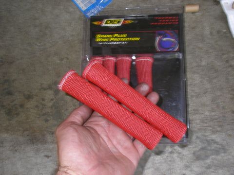 1990 Ford Bronco - Red spark plug wire protection sleeves are shown in their packaging, with a hand holding two of the sleeves.