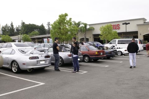 2006 Cadillac STS - A parking lot scene with multiple vehicles and pedestrians under an overcast sky.