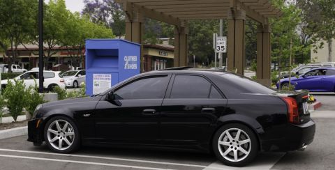 2006 Cadillac STS - A black Cadillac sedan is parked in a lot next to a blue donation bin.