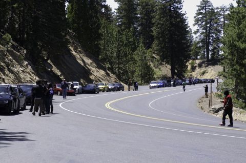 2006 Cadillac STS - A gathering of vehicles parked along a scenic mountain road, with people observing the cars.