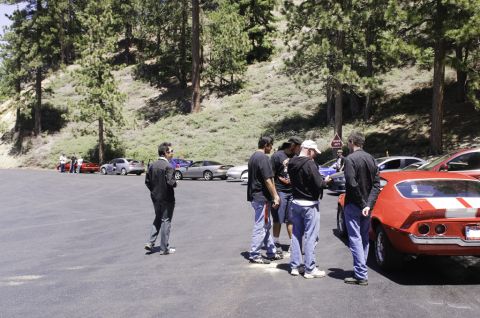 2006 Cadillac STS - A group of people stand around a red muscle car with white racing stripes in a parking lot.