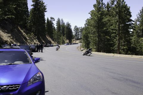 2006 Cadillac STS - Motorcycles speed along a scenic, winding mountain road, with parked cars and spectators on the side.