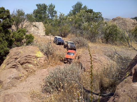 1988 Ford Bronco - Three remote-controlled vehicles navigate a , dry terrain with sparse vegetation and large rocks.