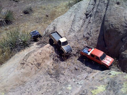 1988 Ford Bronco - Several RC trucks navigate a , outdoor environment with rocks and sparse vegetation.