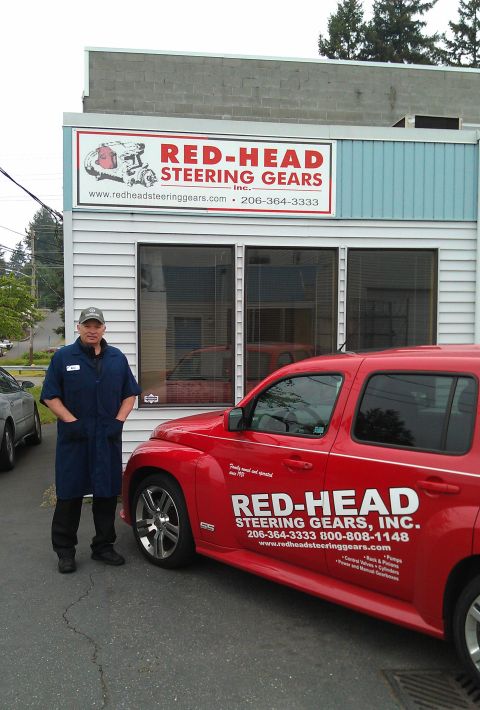 1990 Ford Bronco - A man stands next to a red SUV with company branding outside a building.