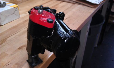 1990 Ford Bronco - A close-up view of a refurbished power steering gearbox, painted black with a red top, resting on a wooden surface.
