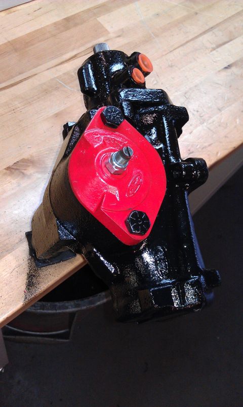 1990 Ford Bronco - A black steering gear assembly with a red accent bracket is shown on a wooden workbench.
