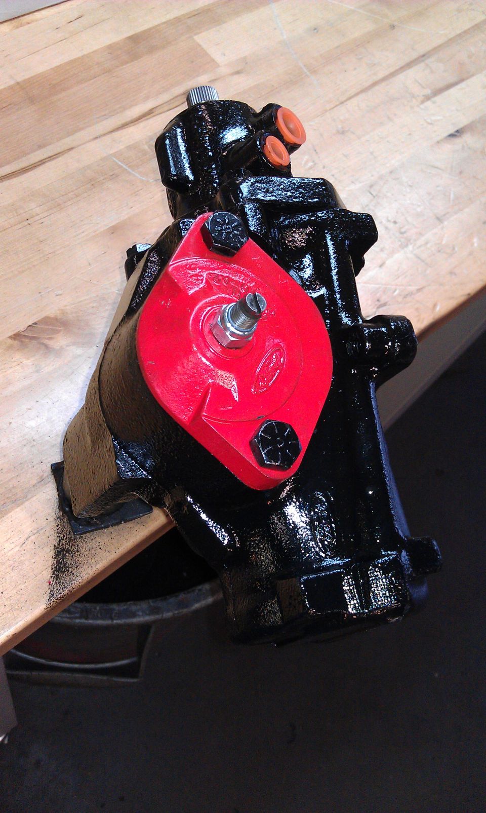 Black steering gear with a red bracket and orange caps on a wooden surface