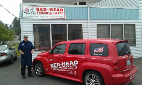 1990 Ford Bronco - A red SUV with the Red-Head Steering Gears logo and an American flag sticker is parked in front of the business.