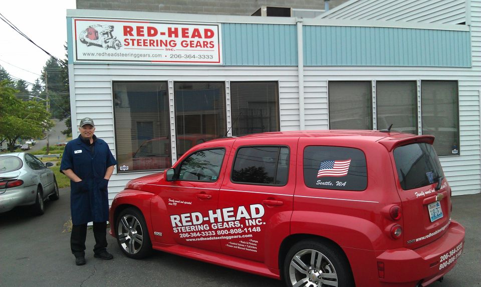 Red SUV with Red-Head Steering Gears logo and American flag sticker parked outside business