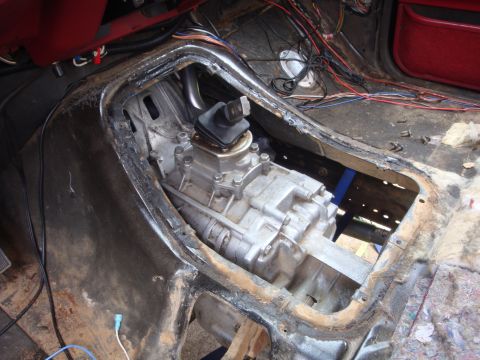 1989 Ford Bronco - The interior of a vehicle is shown with the transmission and transfer case removed, revealing exposed wiring and the floor structure.
