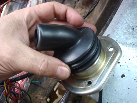 1989 Ford Bronco - A hand holds a black rubber boot over a metal mounting plate.