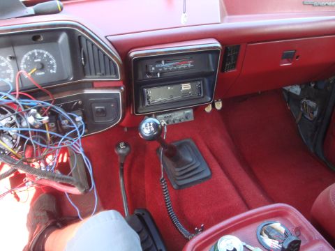 1989 Ford Bronco - The interior of a vehicle shows a manual transmission and a dashboard with exposed wiring.