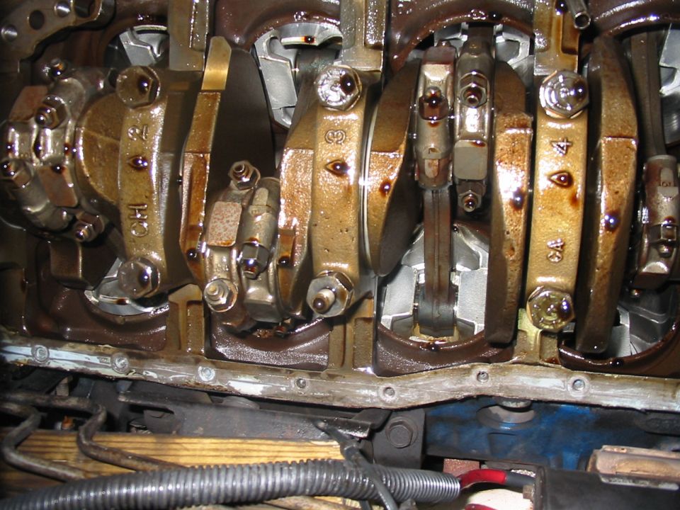 Engine crankshaft with connecting rods and bearings, showing oil. Some rods have numbers like '3' and '4'