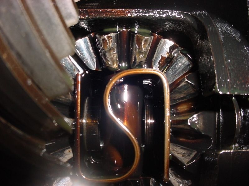 Close-up of differential spider gears and S-shaped retaining clip inside an oily axle housing