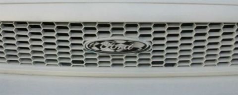 1998 Ford Crown Victoria - Close-up of a white 1998 Ford Crown Victoria's front grille, the iconic Ford oval emblem.