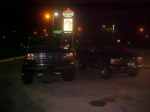 1996 Ford Bronco - Two Ford Broncos are parked at a gas station at night, with the Amoco sign visible.