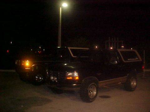 1996 Ford Bronco - Two SUVs are parked side-by-side at night, illuminated by a nearby street light.