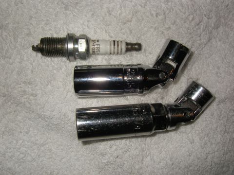 1990 Ford Bronco - A single spark plug and two chrome swivel socket wrenches are laid out on a textured white surface.