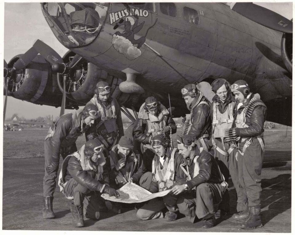 Bomber aircraft with nose art 'HELL'S ANGELS' and crew gathered around a map