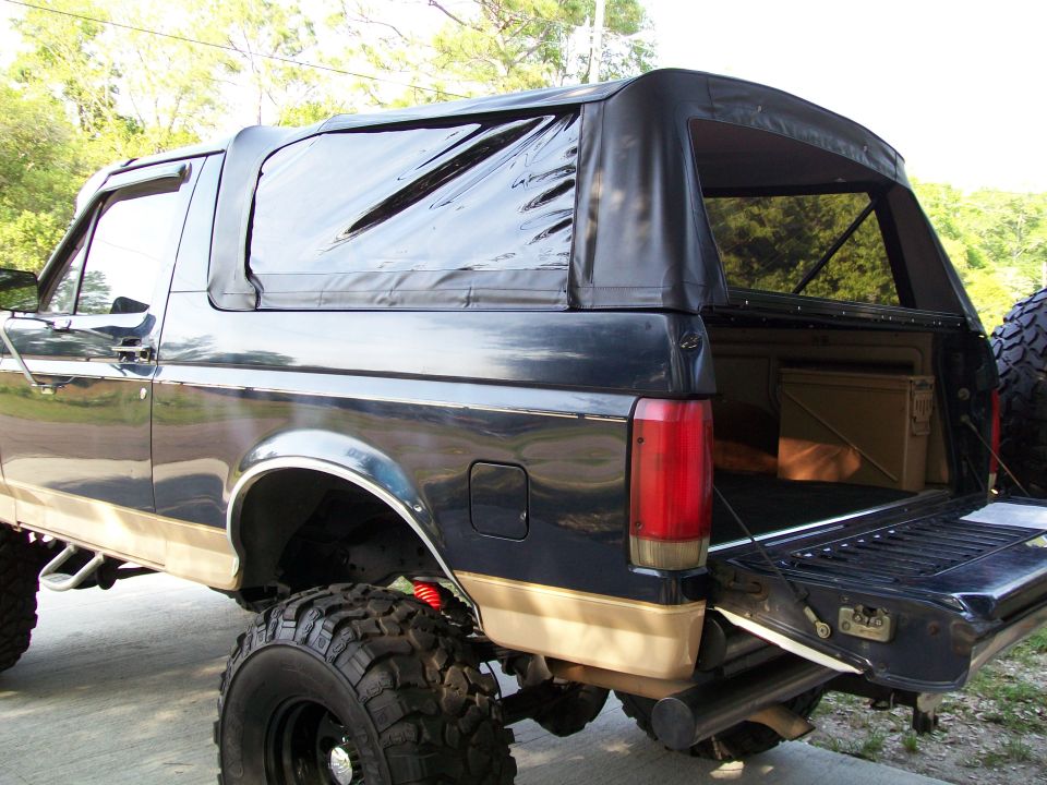 Black Ford Bronco with tan lower body trim and a soft top, rear view with tailgate open