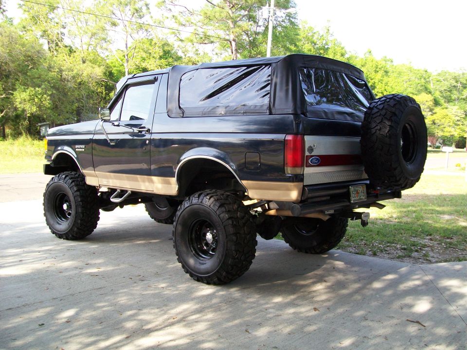 Lifted black and tan Ford Bronco with soft top, big mud tires and rear spare