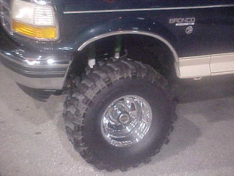 1996 Ford Bronco - A dark blue Ford Bronco is shown with large off-road tires and chrome rims.