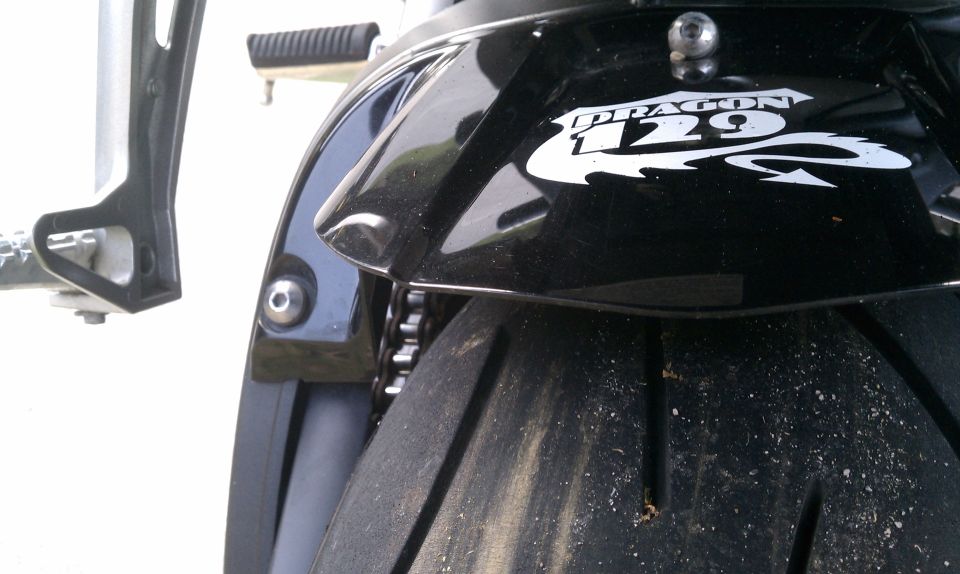 Black motorcycle rear fender with white 'DRAGON 129' graphic and tire. Supermotors.net logo visible