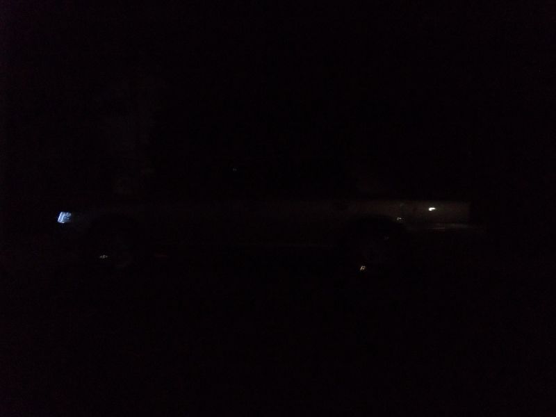 Very dark night side view of a sedan with faint body outline and a blue glow