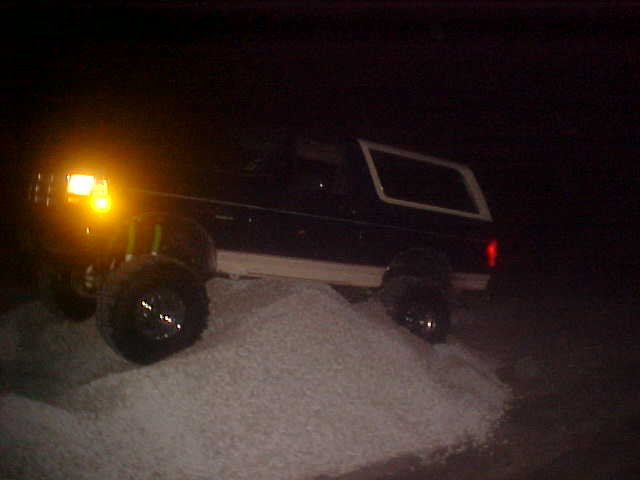 1996 Ford Bronco with headlights on, driving up a pile of white material at night