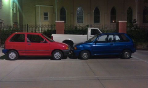 1991 Ford Festiva - Two subcompact hatchbacks, a red 1991 Ford Festiva and a blue car, are parked side-by-side.