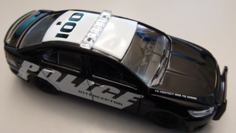 1993 Ford Taurus - A black police car toy with 'POLICE INTERCEPTOR' markings and a light bar is shown from a high angle.