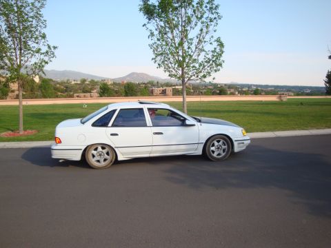 1990 Ford Taurus - A white 1990 Ford Taurus sedan with a contrasting black hood is seen from the side on a paved road.