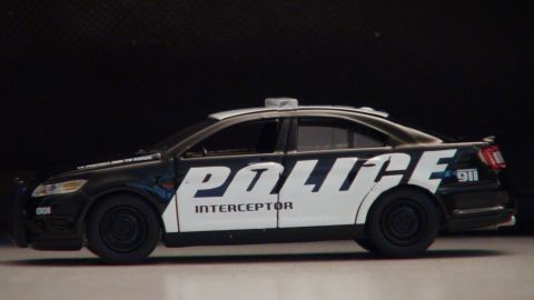 1993 Ford Taurus - A black and white police car toy is shown from the side against a dark background.