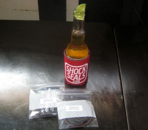 1996 Ford Bronco - A beer bottle with a lime wedge sits in a red koozie next to two plastic bags containing automotive parts.