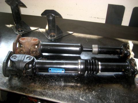 1996 Ford Bronco - Two driveshafts and mounting brackets are laid out on a workbench, one driveshaft has a visible brand sticker.