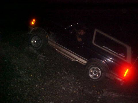 1996 Ford Bronco - A dark Ford Bronco navigates a rocky terrain at night, its lights illuminating the path ahead.