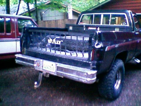 1983 Chevrolet C/K Pickup - The rear of a black 1983 Chevrolet C/K Pickup is shown, a 'BULLY' tailgate insert and a spare tire in the bed.