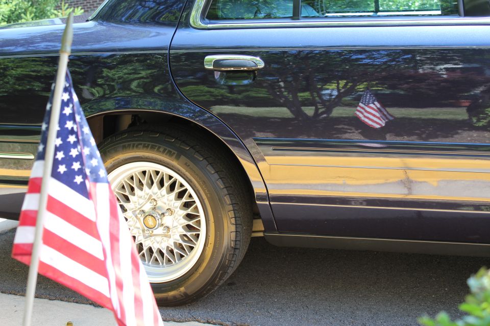 1999 Ford Crown Victoria side view with American flag on pole and reflected in door