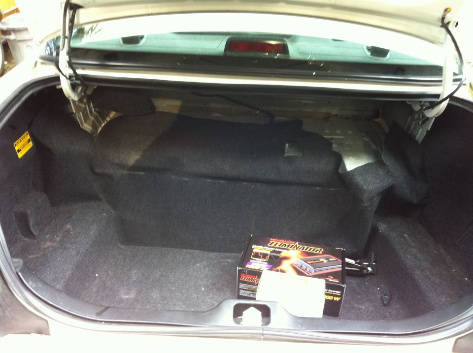 Trunk interior of a 2005 Ford Crown Victoria with a large subwoofer box and an amplifier box. The trunk carpet is gray