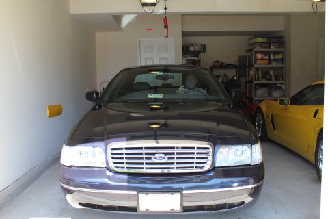 1999 Ford Crown Victoria - A dark sedan is parked in a garage, with a yellow sports car visible to its right.
