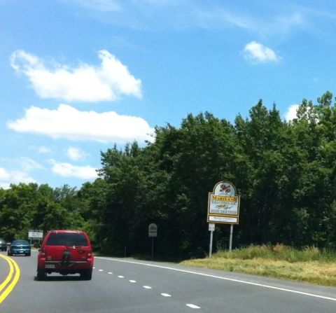 1999 Ford Crown Victoria - A red SUV drives on a highway past a Maryland welcome sign.