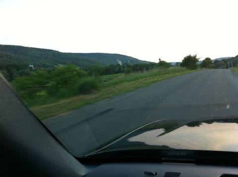 1999 Ford Crown Victoria - View from inside a vehicle traveling on a road through a scenic, hilly landscape.
