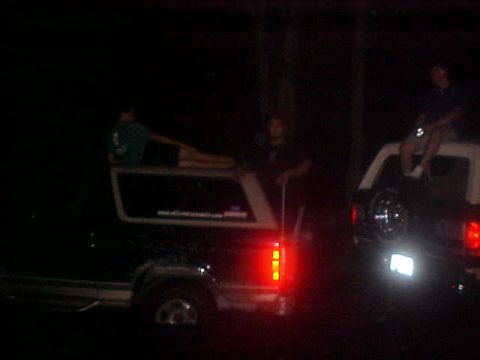 1996 Ford Bronco - Two SUVs are parked at night, with people relaxing on their roofs.