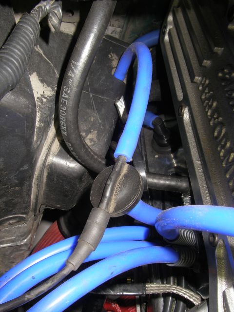 1990 Ford Bronco - Tight engine-bay close-up of blue aftermarket spark plug wires routed past a black plug boot and a rubber-capped fitting stamped "3889746",…