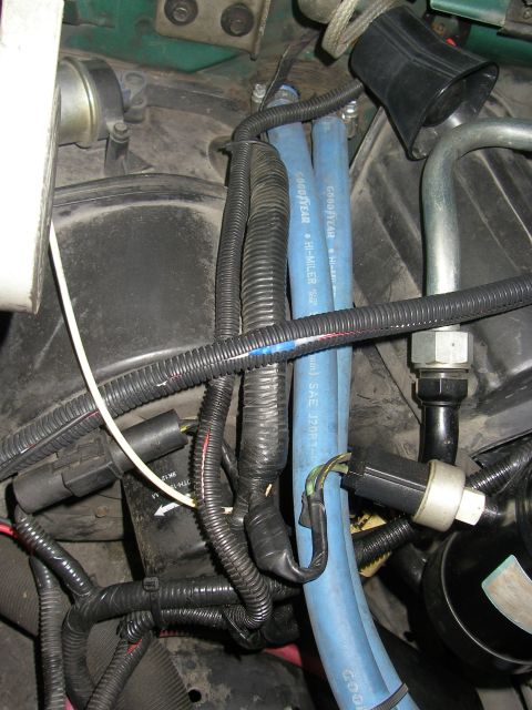 1990 Ford Bronco - Close-up of an engine bay showing a blue Goodyear Hi-Miler heater hose routed alongside black corrugated wiring looms, metal fittings, and…