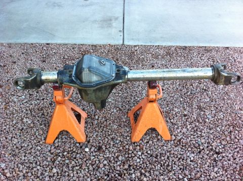 Suzuki Samurai - A bare front differential housing and axle tubes resting on two orange jack stands atop pink gravel beside a concrete slab. The cast center…
