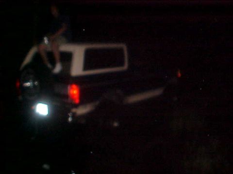 1996 Ford Bronco - A person sits atop a pickup truck's camper shell at night.