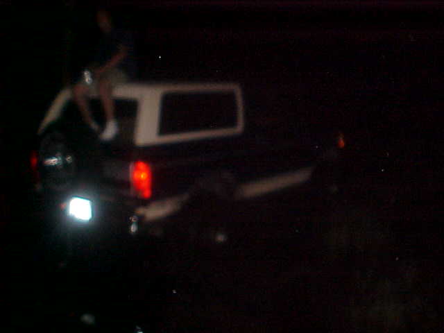Rear of pickup truck with white camper shell, person sitting on top